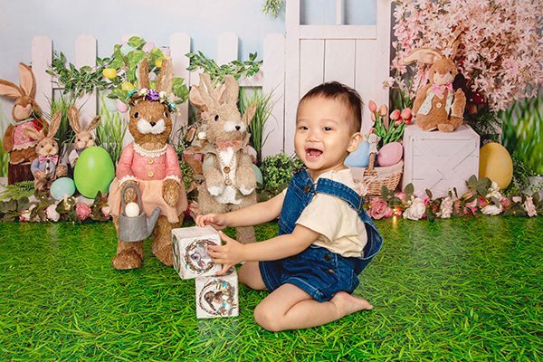 A little boy is sitting on the grass playing with blocks and stuffed animals.