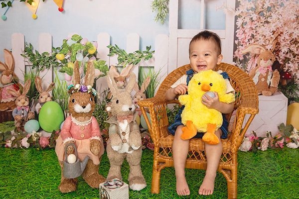 A little boy is sitting in a wicker chair holding a stuffed chicken.