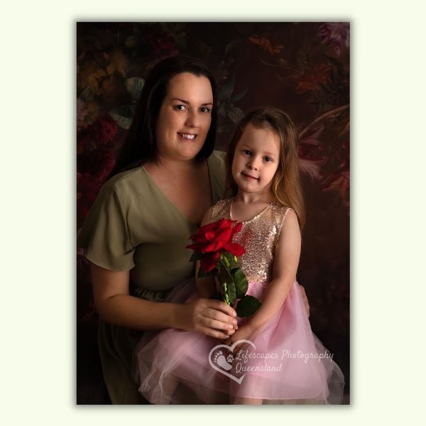 A woman and a little girl are posing for a picture and the little girl is holding a red rose