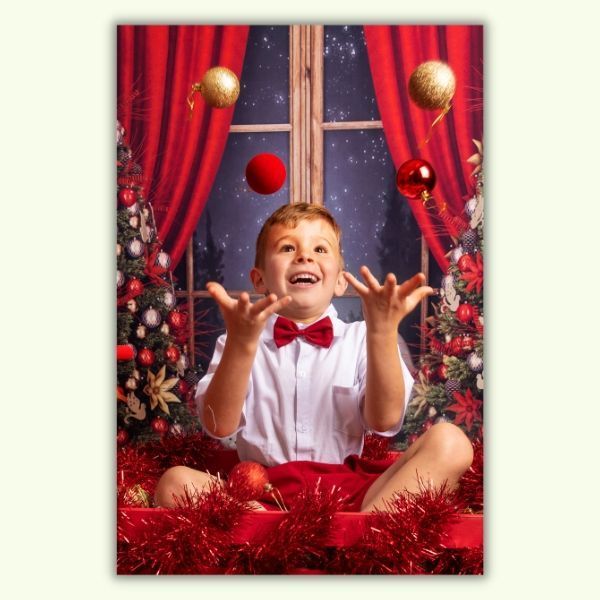 A young boy is juggling christmas balls in front of a window