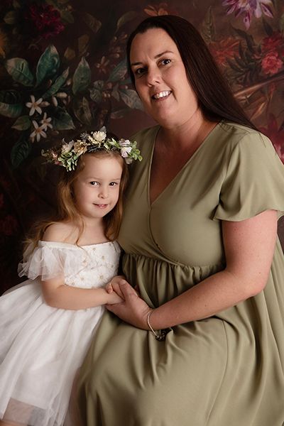 A woman and a little girl are posing for a picture . the little girl is wearing a flower crown.