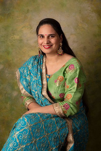 A woman in a green and blue dress is sitting down and smiling.
