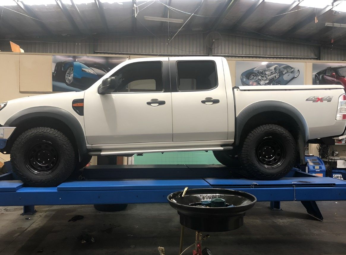 A White Truck is Sitting on a Lift in a Garage — Autochange Mechanical Repairs & Tyres in Bellambi, NSW