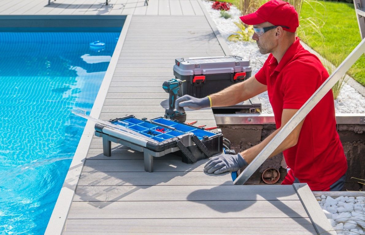 Worker in red shirt installing poolside deck tiles beside a swimming pool