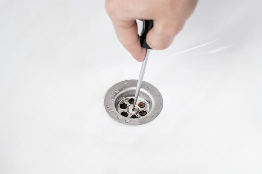 a person is using a screwdriver to fix a sink drain .
