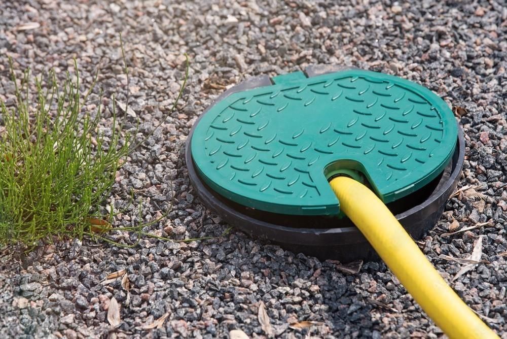 a green manhole cover with a yellow hose attached to it .