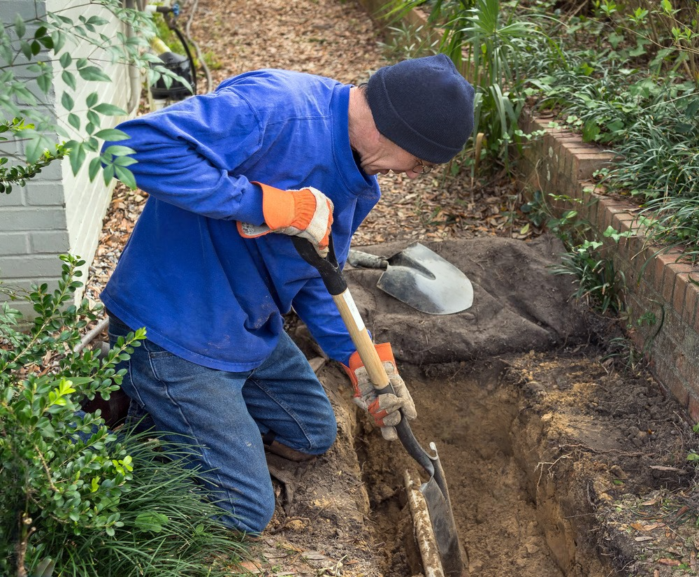 a man is kneeling down and digging a hole with a shovel .