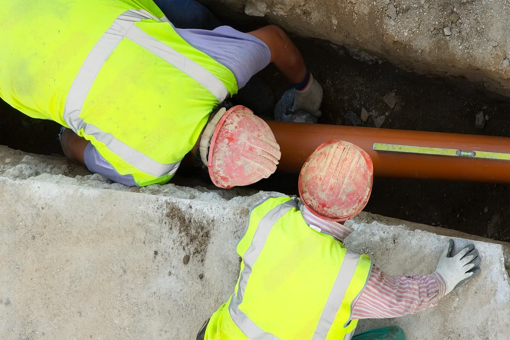 two construction workers are working on a pipe in a trench .