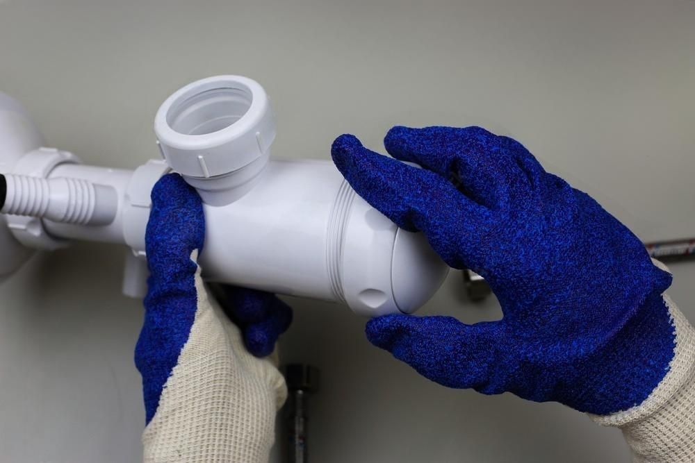 a person wearing blue gloves is fixing a pipe .
