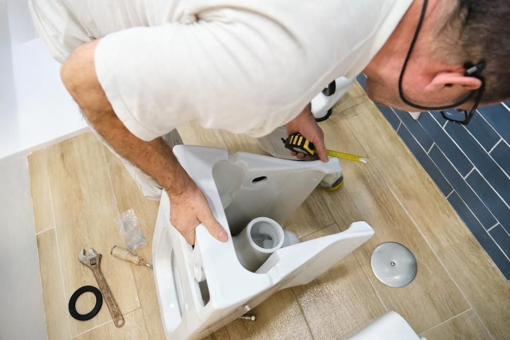 a man is measuring a toilet with a tape measure in a bathroom .