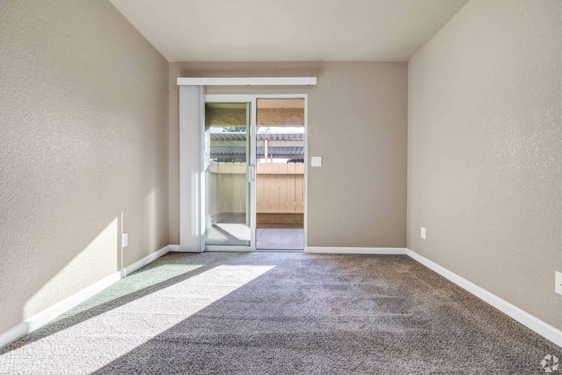 Empty room with sliding glass door to small outdoor area; gray carpet, beige walls.