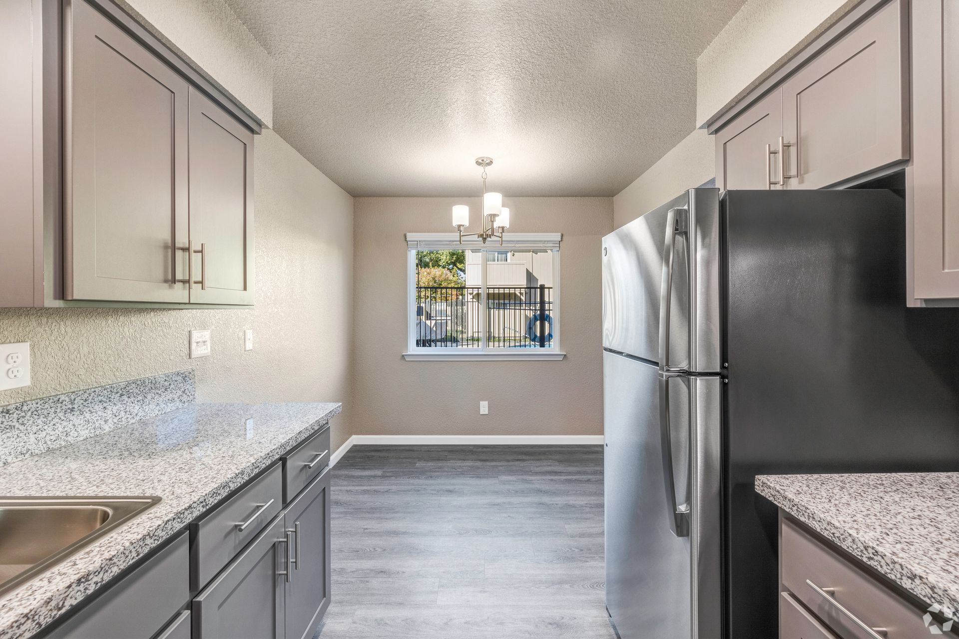 Kitchen with gray cabinets, granite countertops, stainless steel fridge, and a dining area.