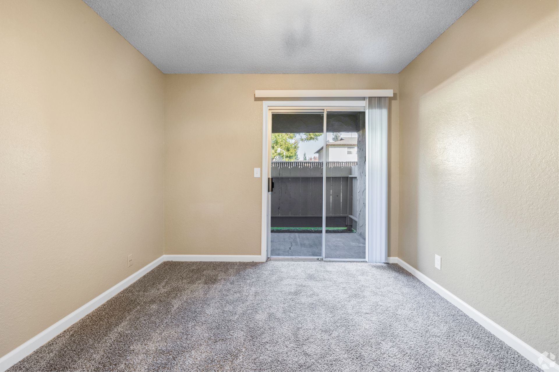 Empty room with carpet, sliding glass door to a patio, and beige walls.