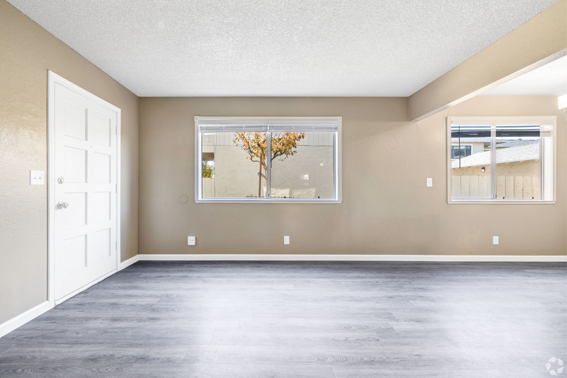 Empty room with beige walls, gray flooring, white door and windows.