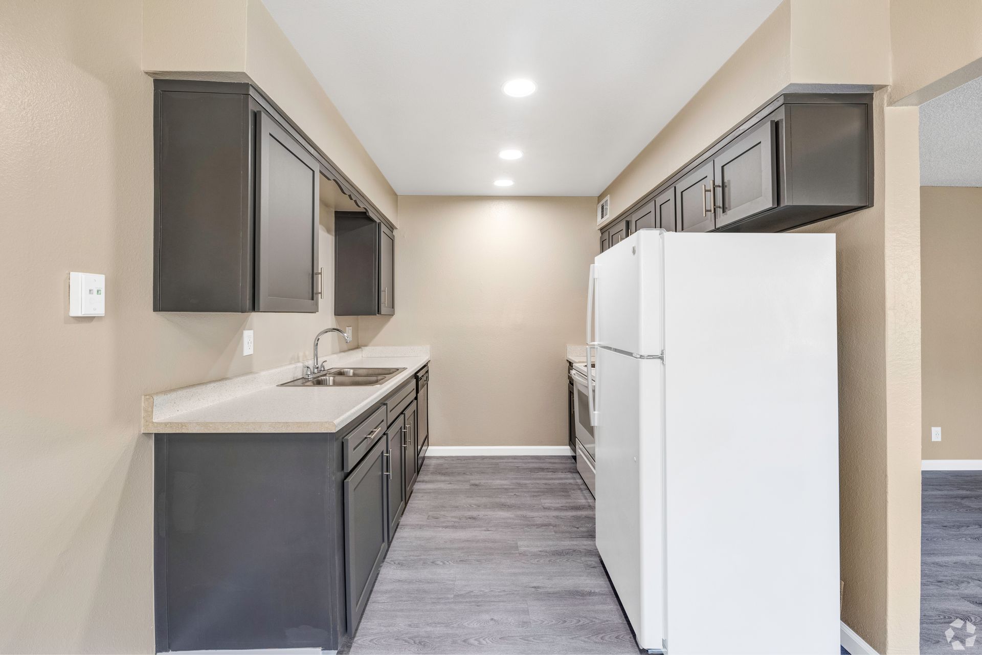 Dark gray kitchen cabinets, gray counters, white appliances in narrow kitchen.