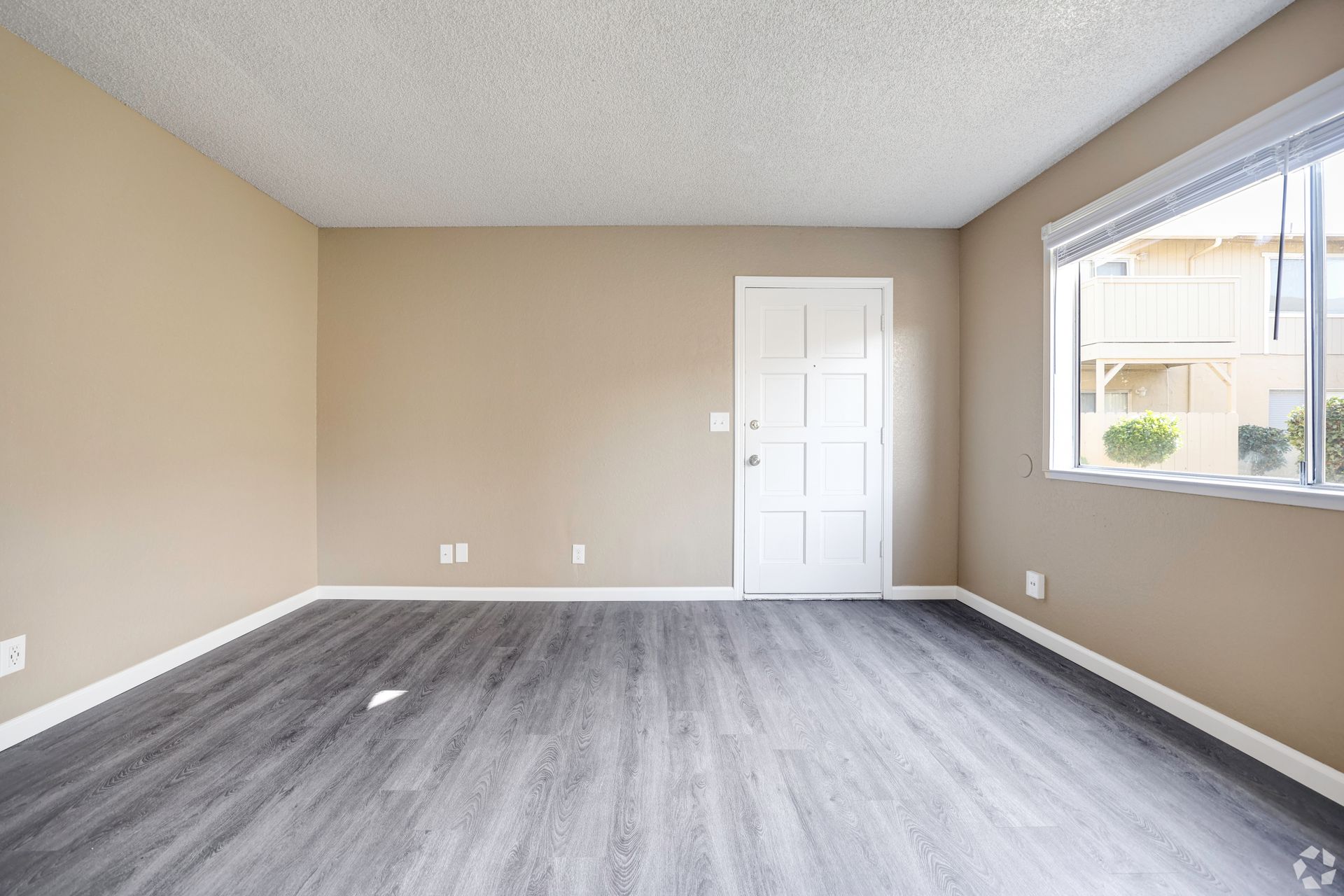 Empty room with wood-look flooring, beige walls, white door, and window with blinds.