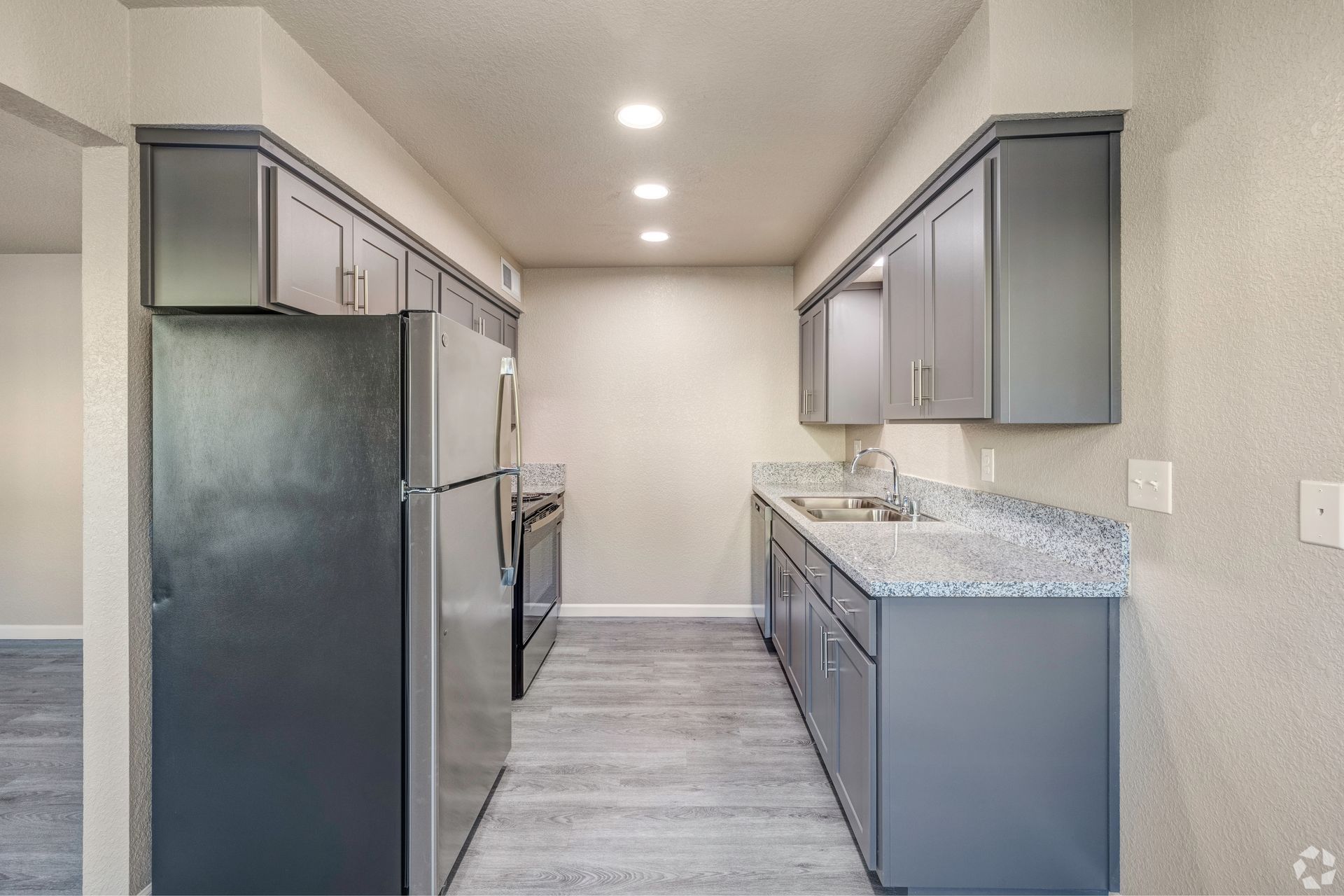 A narrow, modern kitchen with gray cabinets, stainless steel appliances, and speckled countertops.