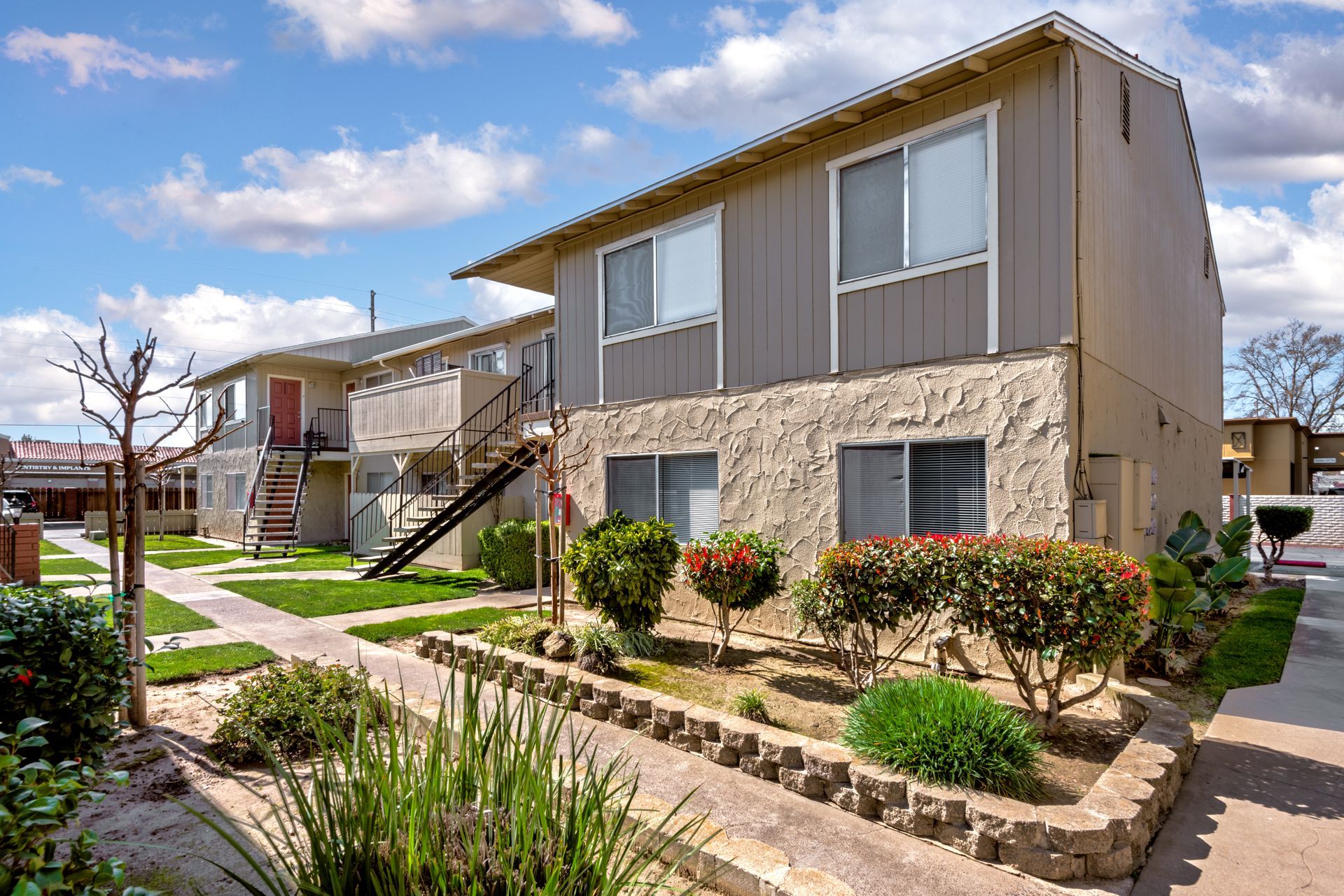 Two-story beige apartment buildings with landscaping under a blue sky.