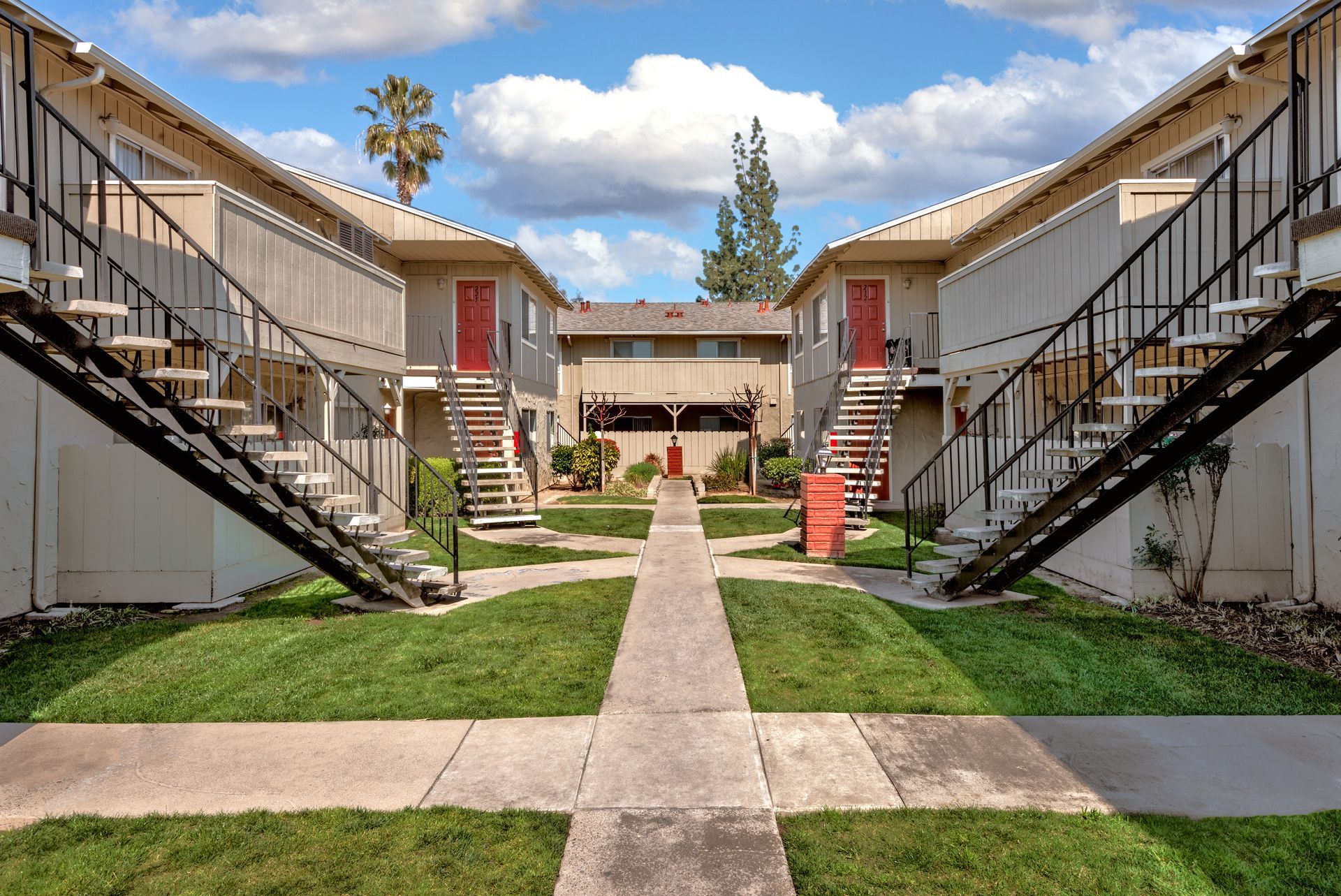Two-story apartment buildings with black staircases facing each other across a grassy courtyard with a walkway.