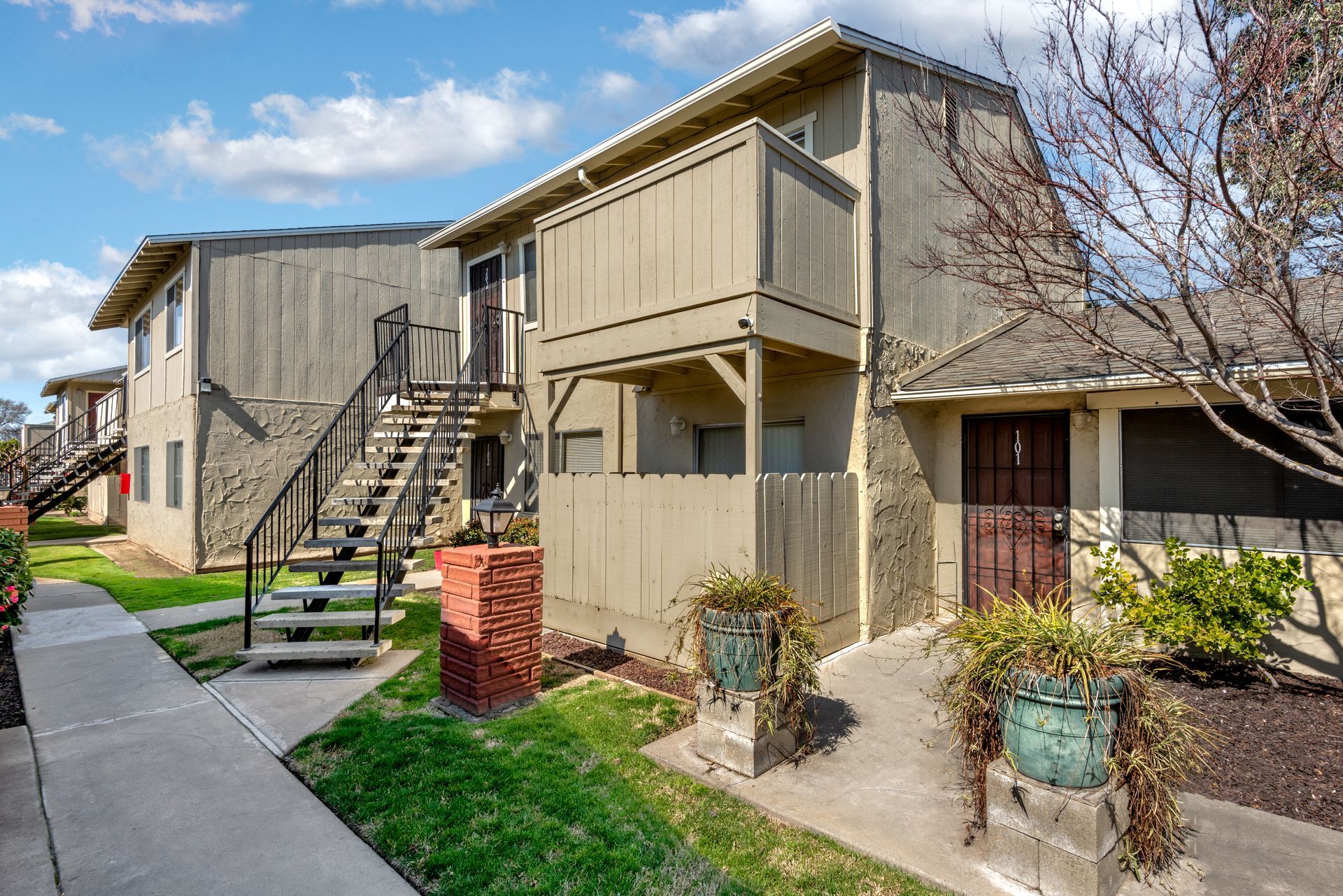 Apartment building with stairs, balconies, and green grass under a blue sky with clouds.
