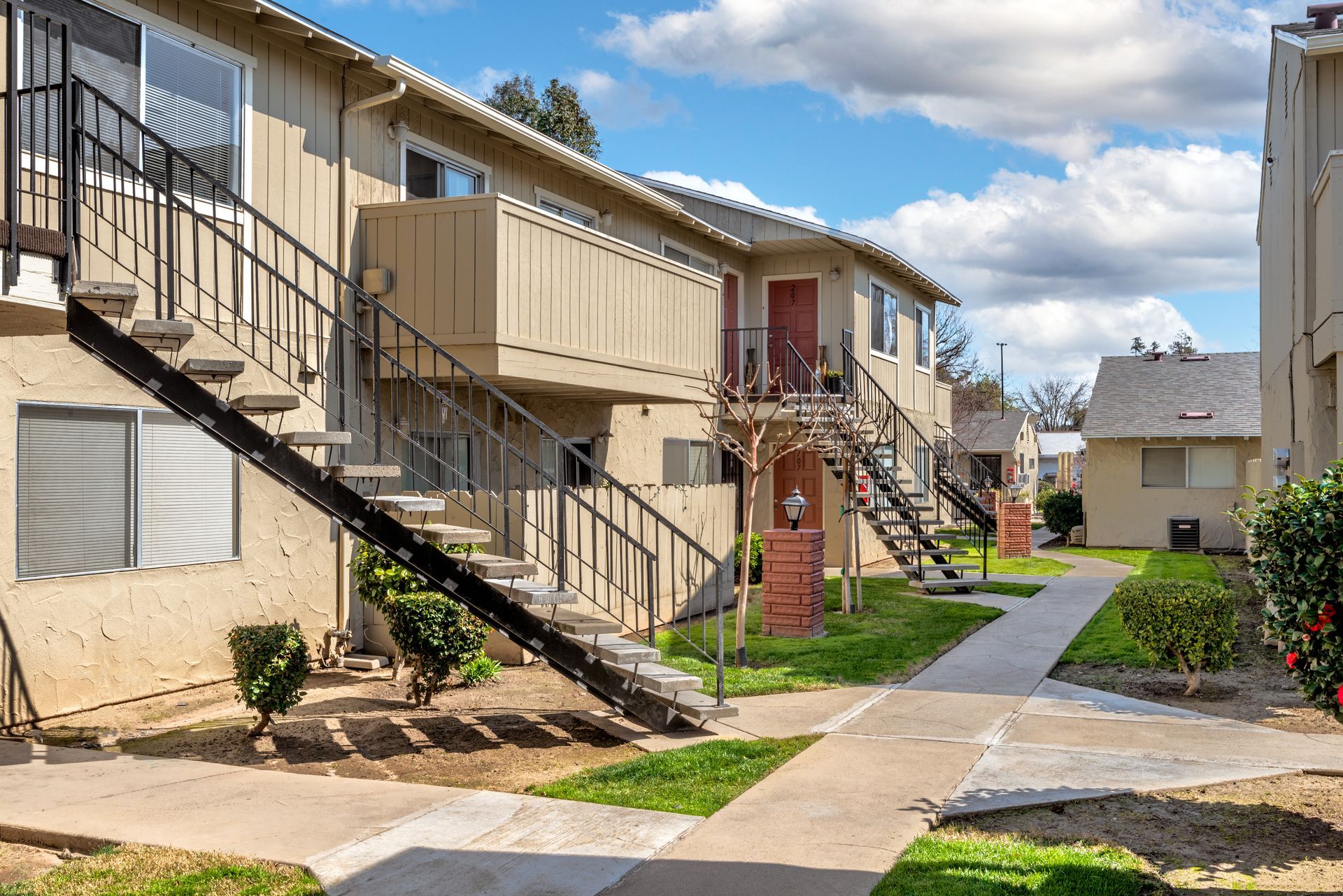 Apartment complex exterior with beige buildings, outdoor staircases, and a paved walkway.