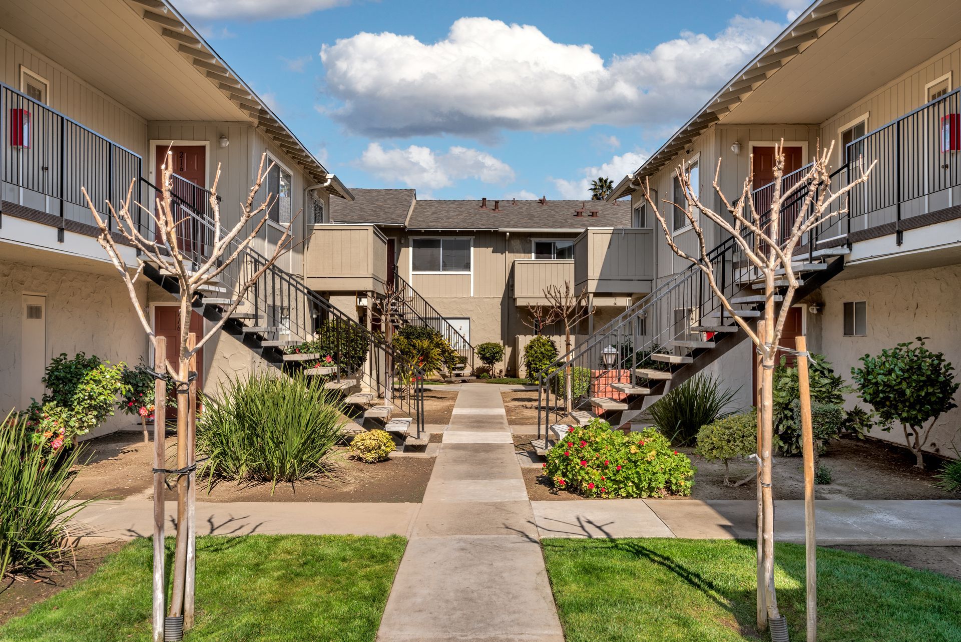 Courtyard of a two-story apartment complex with walkways, landscaping, and a cloudy sky.