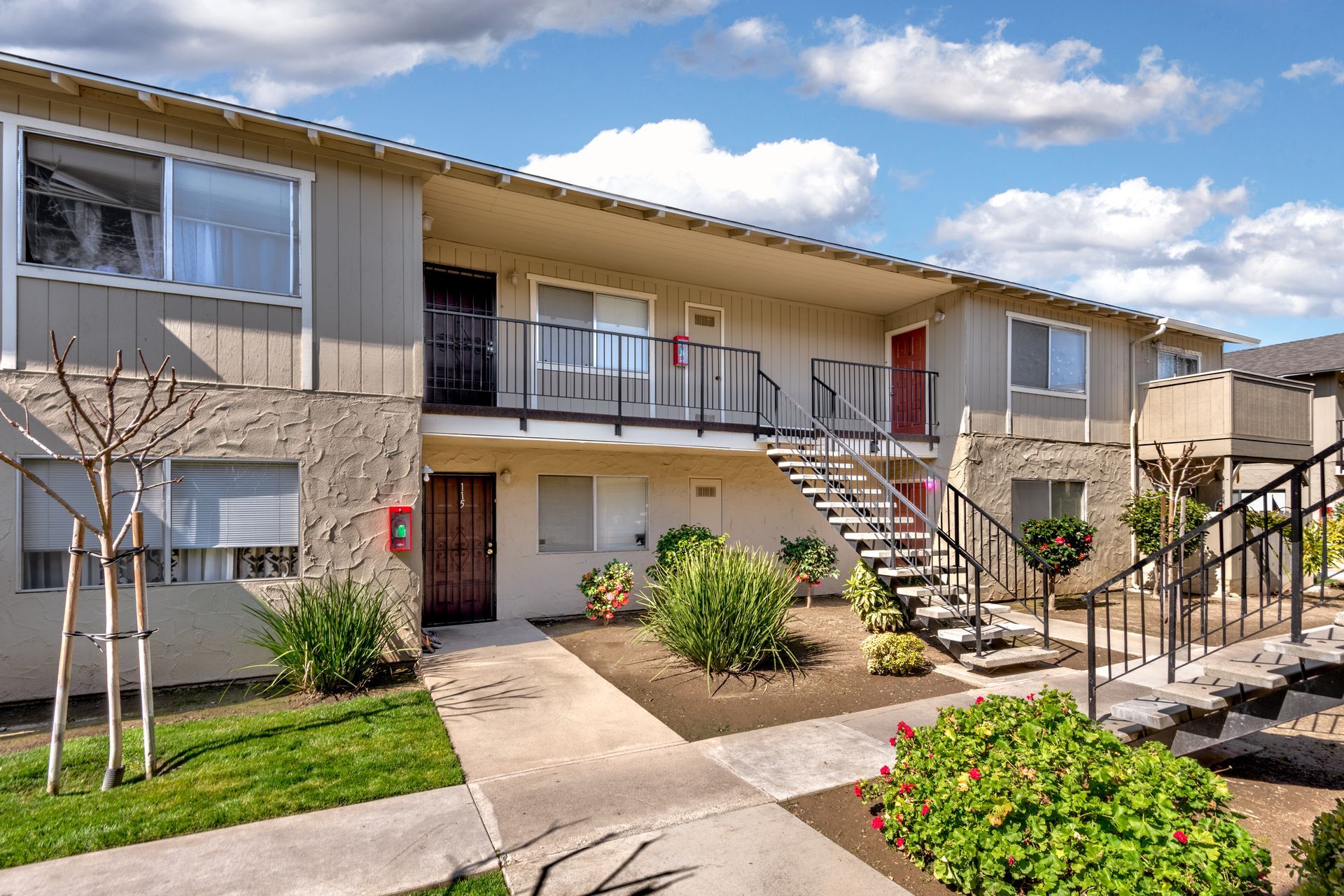 Two-story apartment building with beige siding, outdoor staircases, and a blue sky background.