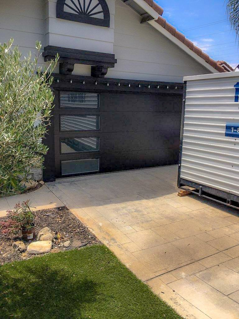 A white house with a black garage door and a white trailer parked in front of it.