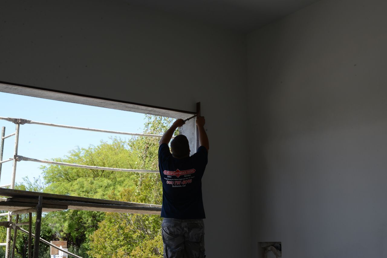 A man in a blue shirt is measuring a garage door opening.