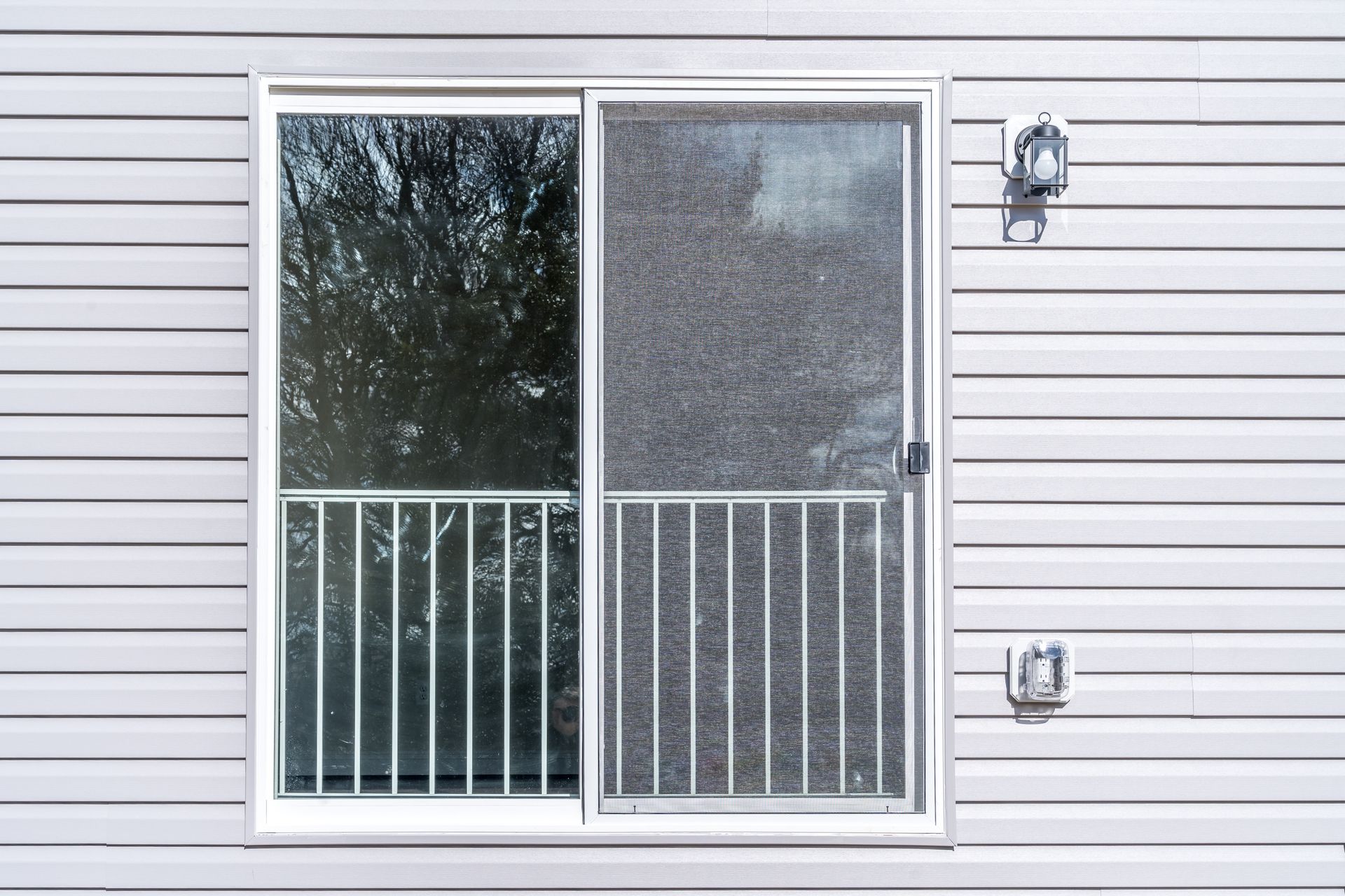 Sliding glass door with blinds and two wall lanterns on white siding.
