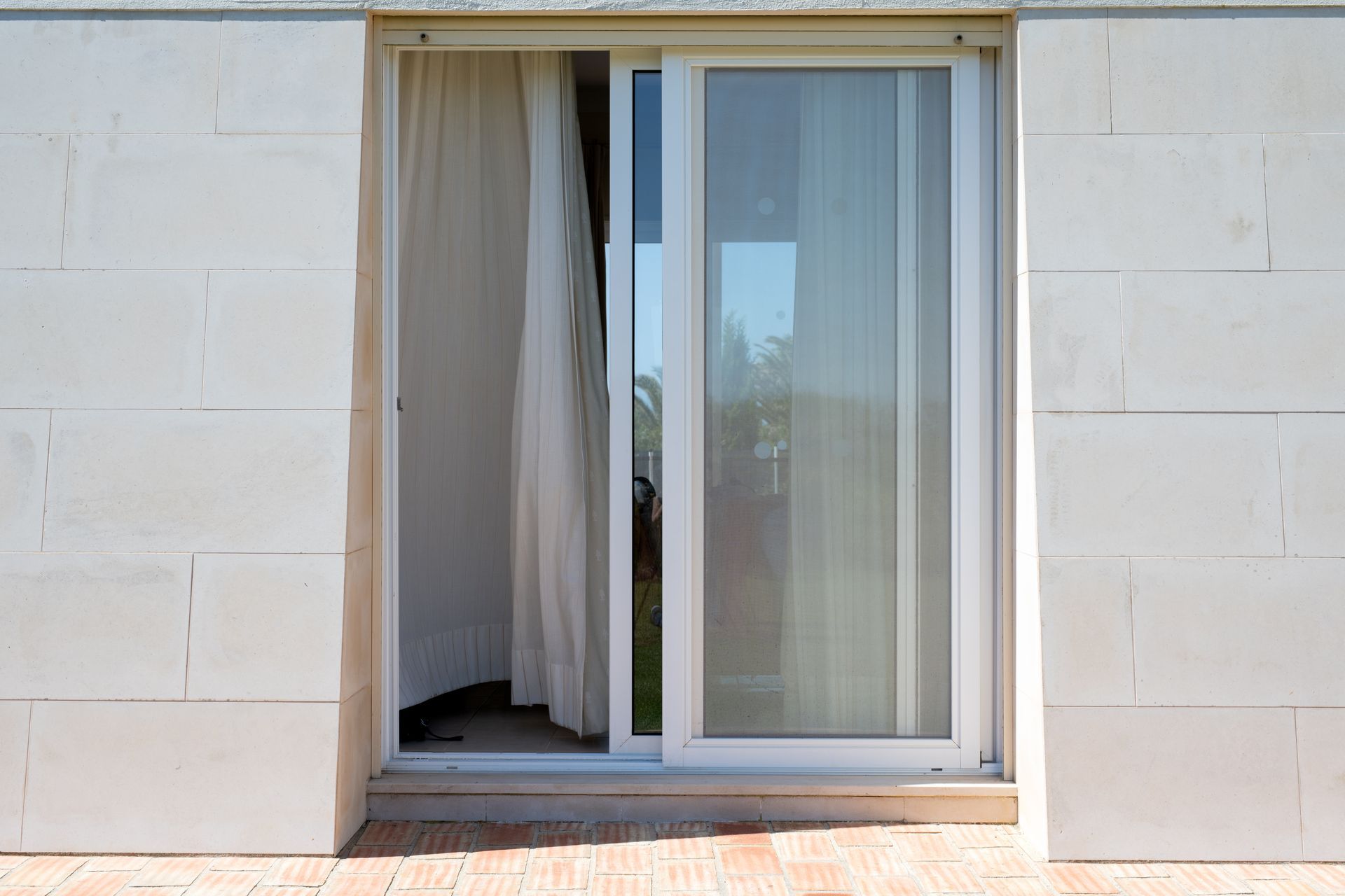 Sliding glass door with sheer curtain in a beige wall opening onto a patio