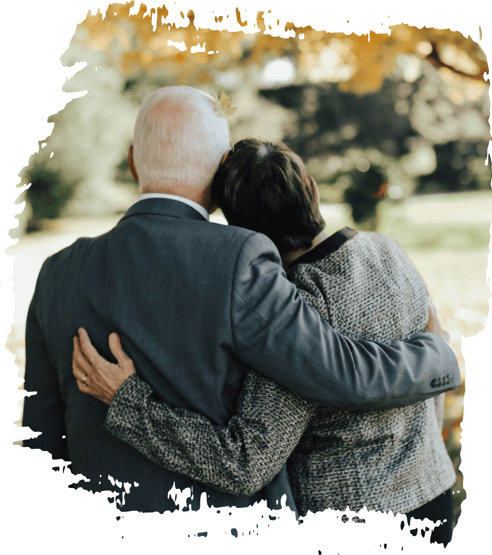 Two people in dark clothing embrace from behind outdoors, framed by a soft brush-stroke border.