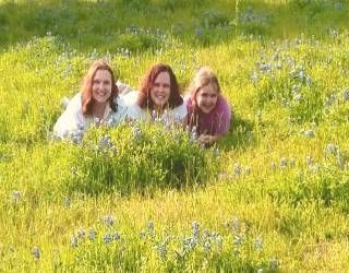 Three people lying in a grassy field with yellow wildflowers, smiling at the camera