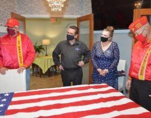 Masked people stand around a red-and-white striped flag draped over a table indoors.