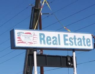 Real estate sign in blue and white on a pole against a clear sky