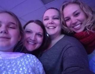 Four smiling friends posing close together in purple lighting, one wearing a red scarf.