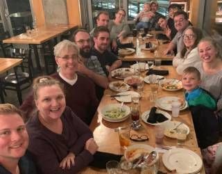 Group of people smiling around a long restaurant table with drinks and plates during a meal