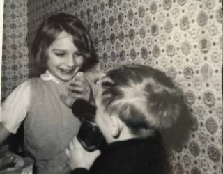 Two children laughing and playing with a toy in front of patterned wallpaper.