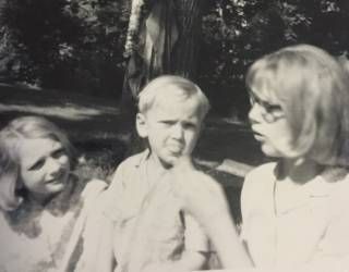 Three people outdoors in a sunny park, with trees in the background.