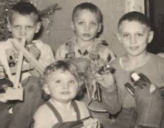 Four children posing indoors with toy vehicles, black-and-white photo.
