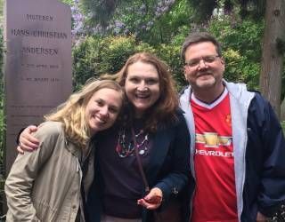 Three smiling people posing outdoors beside a stone memorial