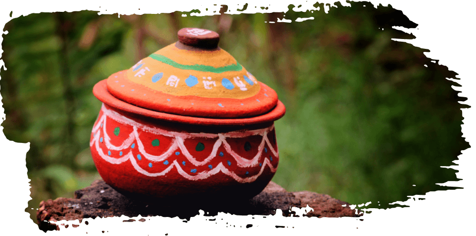 Colorful painted clay pot with floral patterns on a rustic surface, set against a blurred green background
