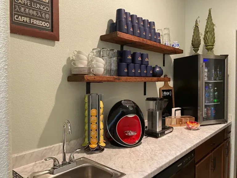 Coffee station with shelves of blue mugs, espresso machine, and mini fridge on a countertop