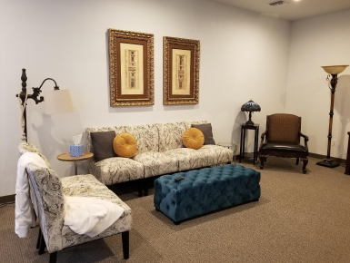Cozy living room with beige sofa, teal ottoman, framed art, lamps, and a chair in the corner