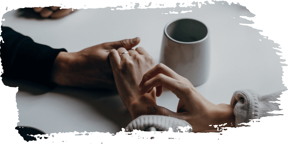 Hands holding in a soft, intimate moment beside a white mug on a table