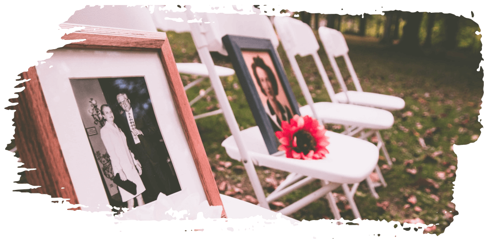Framed wedding photos on white chairs with red flowers outdoors on grass