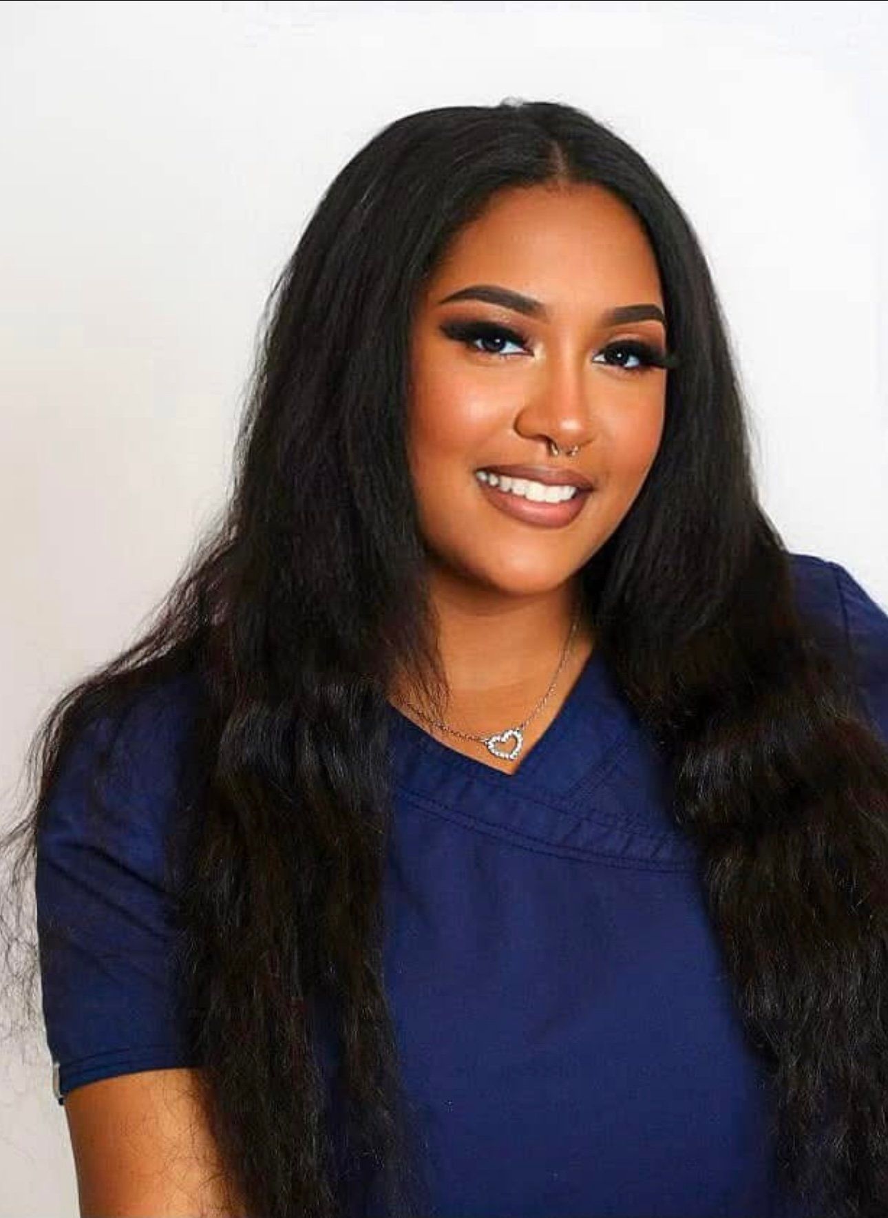 A woman with long black hair is wearing a blue shirt and smiling.