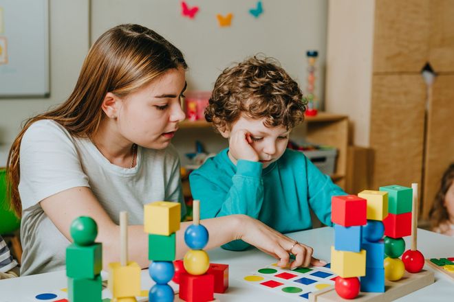 A girl and a boy are playing with blocks at a table.