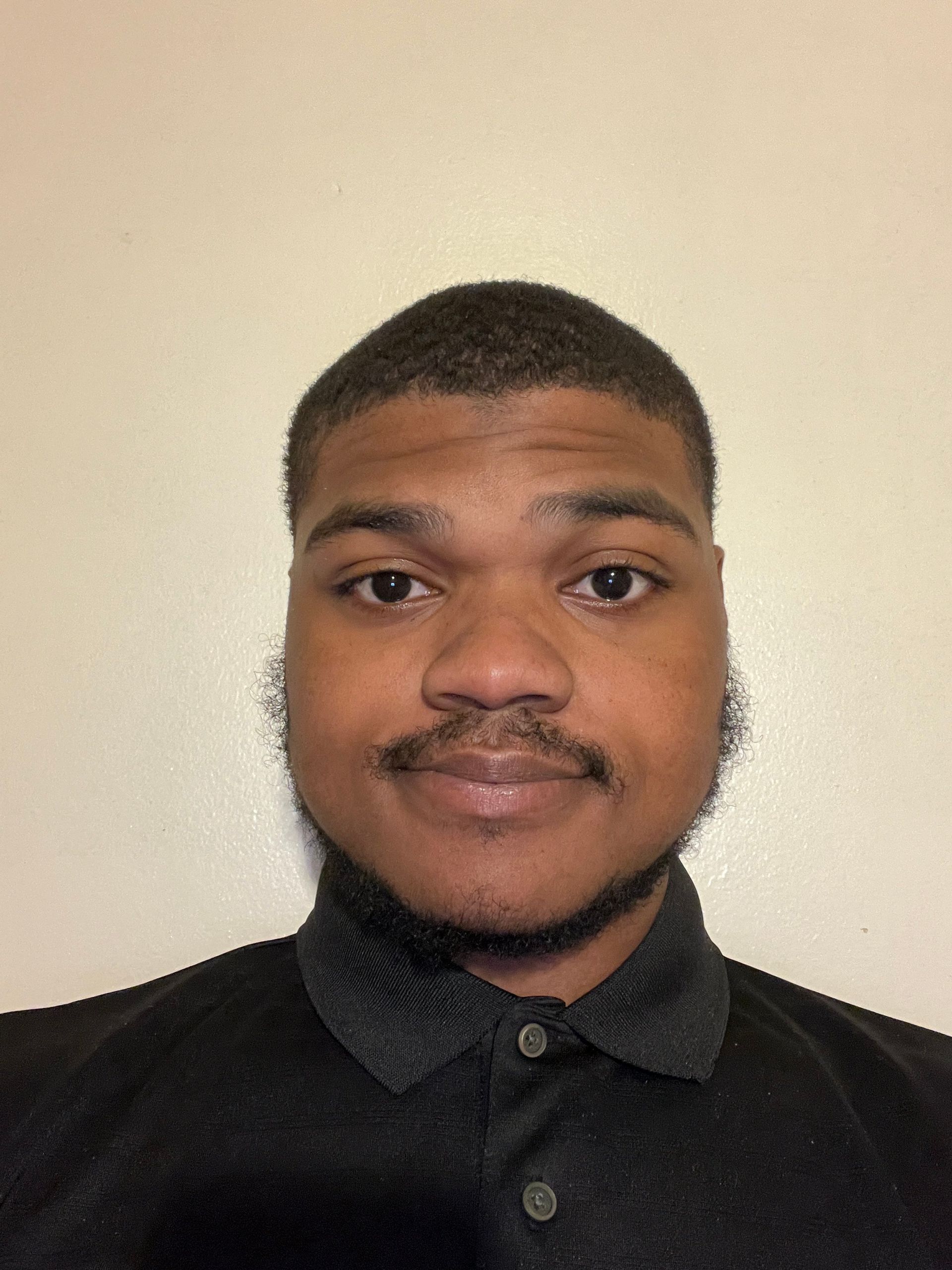 A man with a beard and mustache is wearing a black polo shirt.