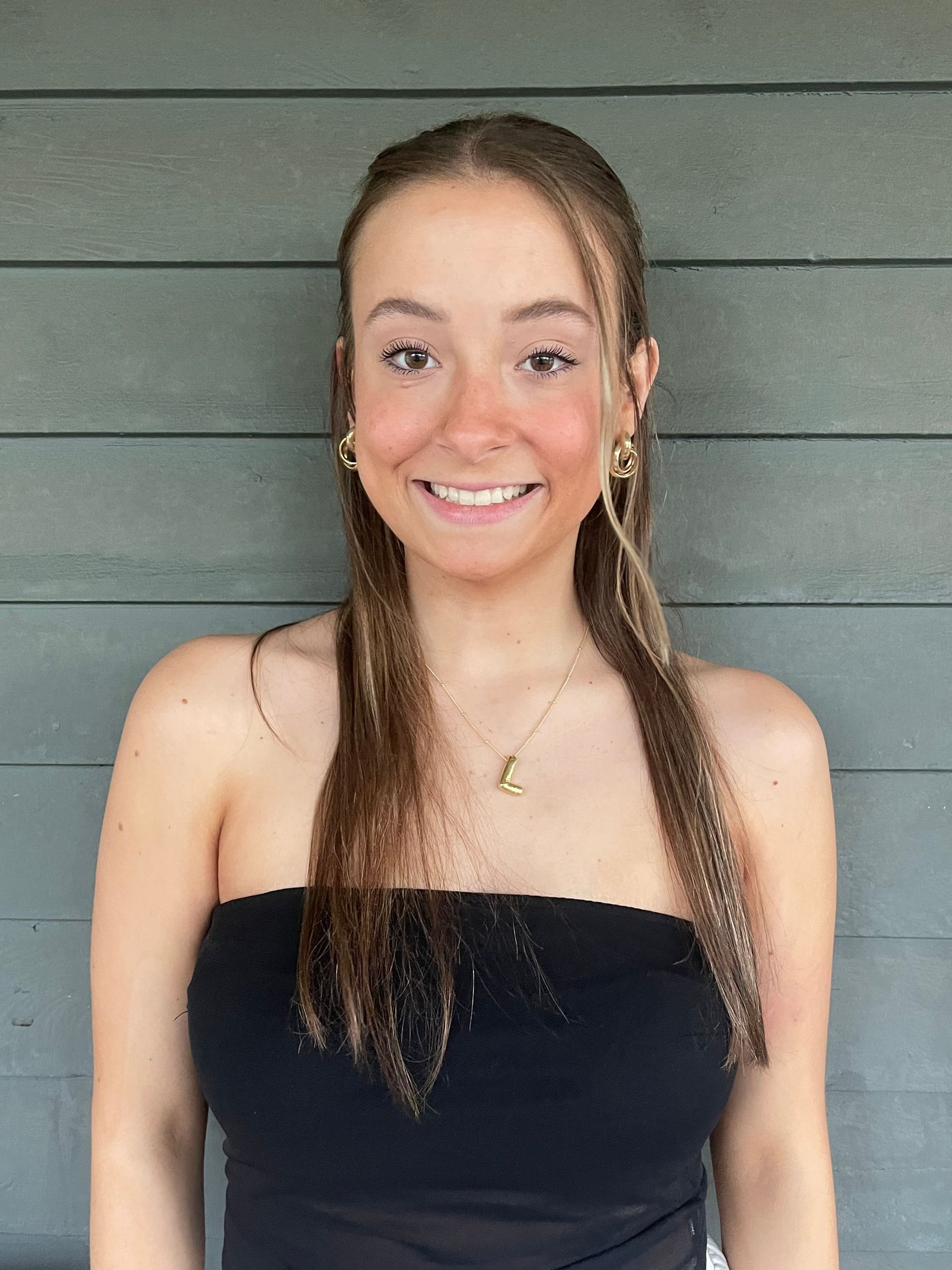 A young woman wearing a black strapless top and earrings is smiling for the camera.
